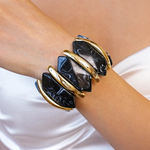 Gros plan d'un large bracelet extensible en résine marbrée noire et barres dorées