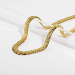 Dettaglio di una collana a catena piatta color oro su un supporto minimalista