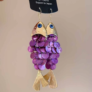 Macro detail of golden fish earrings with shimmering purple shell scales on a display card