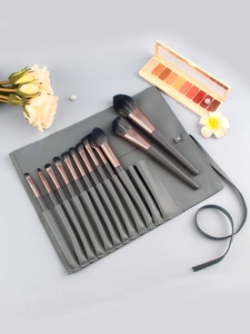 Close-up of 12 professional makeup brushes with rose gold ferrules and a grey leather wrap