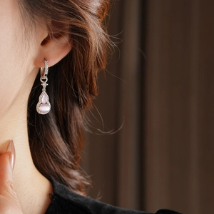 Close-up of a silver gourd-shaped earring with pink stone and clear zircons on a model