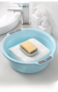 Detail of light blue plastic basin with grey non-slip handles and a soap dish on bathroom counter