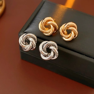 Macro shot of gold and silver Love Knot stud earrings on a black leather jewelry box