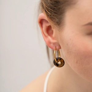 Close-up of model wearing gold hoop earrings with brown tiger eye stone donut pendant