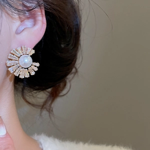 Detailed close-up of a sunflower-shaped gold pearl earring with baguette zircon accents
