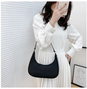 Detail of a black nylon crescent hobo bag worn with a white pleated dress for casual style