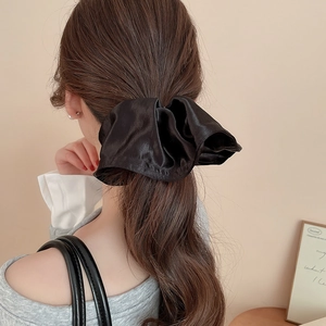 Detail of a large black satin scrunchie shown on a ponytail with a silky texture finish