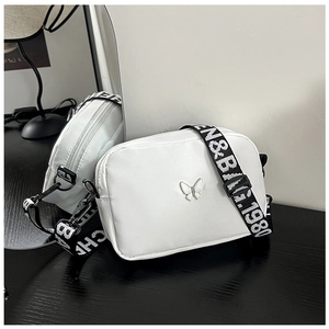 Detail of white nylon crossbody bag with silver butterfly ornament and lettered strap