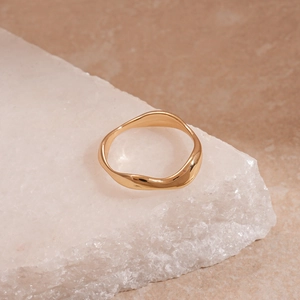 Detailed view of irregular wavy gold ring on white stone texture with minimalist design