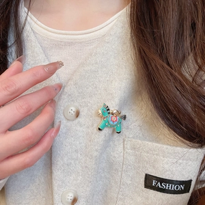 Detailed view of a turquoise enamel horse brooch with floral patterns on a beige cardigan