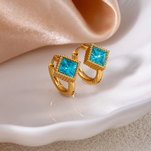 Close-up of gold star earrings with square sky blue crystals on a white ceramic tray