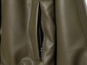 Macro view of side zipper pocket and fine texture on olive green faux leather jacket