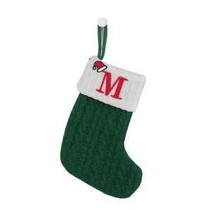 Detail of green knitted Christmas stocking featuring red embroidered letter M and santa hat