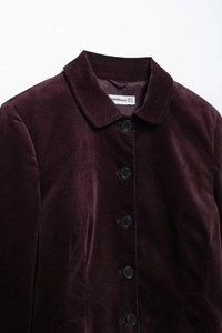 Détail du col d'une veste en velours violet avec bouton noir et étiquette de taille