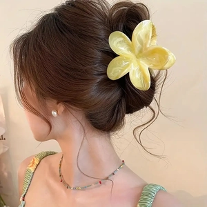 Detail view of yellow plumeria hair claw clip with marble texture on a model ponytail