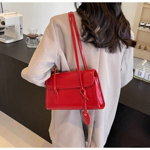Detail of red glossy shoulder bag with heart charm and rectangular flap closure