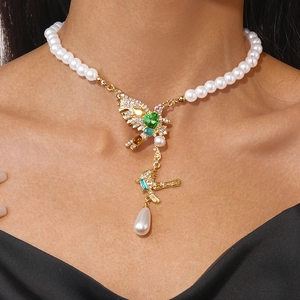 Detailed close-up of pearl necklace featuring a golden bird pendant with green heart gem