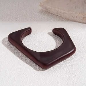 Detail view of a geometric dark reddish-brown acrylic open cuff with a polished finish