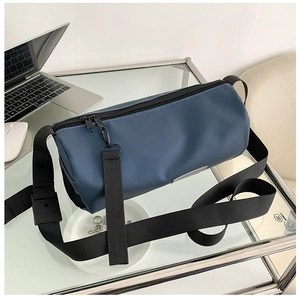 Détail du sac cylindrique bleu marine avec bandoulière réglable sur bureau en verre