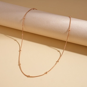 Dettaglio della collana a catena serpente in oro rosa con piccole perle su sfondo neutro