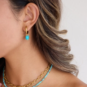 Close-up of 18k gold hoop earrings with turquoise pendants worn by a model in soft light