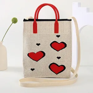 Detail of knit tote bag featuring red and black heart patterns and red round handles