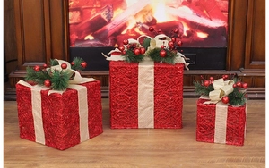 Close-up of three red woven Christmas gift boxes with golden bows and pine needles