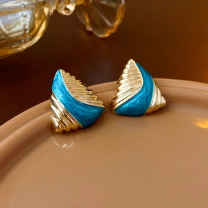 Close-up of vintage gold and blue enamel triangle earrings on a beige ceramic plate