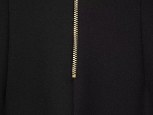 Détail en gros plan de la fermeture éclair dorée sur un pantalon noir à taille haute