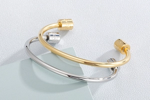 Close-up of gold and silver open bracelets featuring detailed floral engravings on polished steel