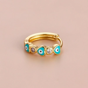 Gold heart earrings featuring blue evil eye enamel and white zircon stones on pink background