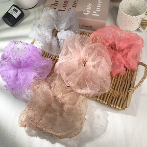 Detail of five polka dot lace scrunchies in pastel colors on a woven tray