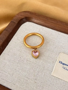 Detail of a golden stainless steel ring with a faceted pink heart-shaped crystal pendant
