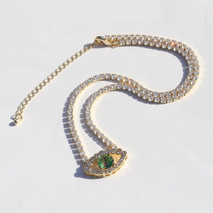Close-up of gold tennis necklace featuring a green zircon evil eye pendant with crystals