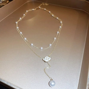 Detail of double-layer gold chain necklace with white camellia and pearl on gold tray