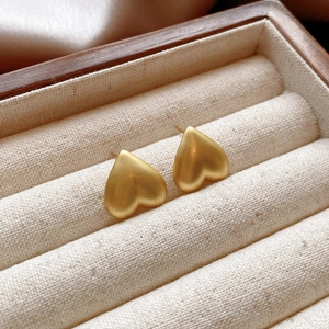 Detailed view of golden matte heart-shaped studs on a minimalist jewelry display