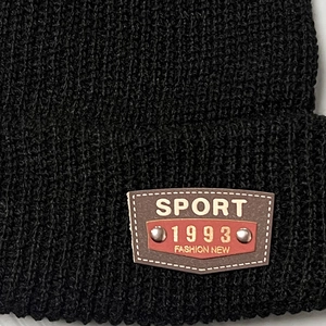 Close-up of black ribbed knit beanie featuring a brown leather patch with silver rivets