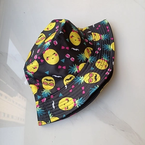 Vue détaillée d'un bob noir avec des motifs d'emojis ananas vibrants sur du marbre