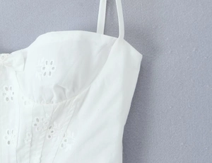 Gros plan détaillé du caraco en dentelle blanche avec broderie florale et fines bretelles