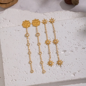 Golden sun and star tassel earrings with cubic zirconia inlay on a stone background