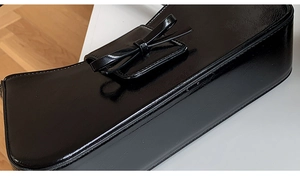 Detail of glossy black patent leather baguette bag with a stylish bow buckle accent