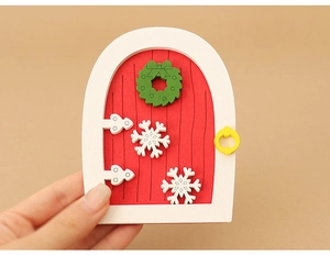 Close-up of a red wooden dollhouse Christmas door with white frame and green wreath