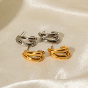 Detailed view of layered C-shaped gold and silver earrings on white silk fabric