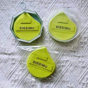 Three lemon green teardrop makeup sponges in various plastic packaging on white cloth