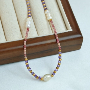 Detail of beaded necklace featuring purple crystals, pink gems, and white baroque pearls