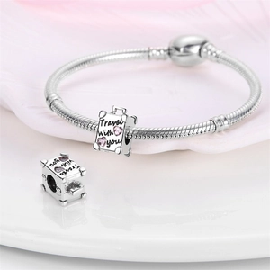Macro detail of silver suitcase charm with pink hearts and Travel with you engraving