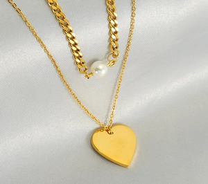 Close-up of golden layered necklace with heart pendant and pearl on silk fabric