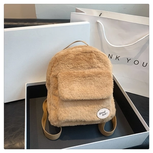 Detalle de mini mochila de felpa caqui con parche bordado dentro de una caja de regalo