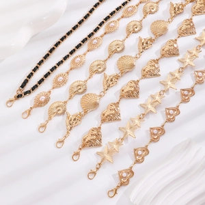 Golden waist chain belts with shells, hearts and pearls on white silk fabric background