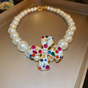 Detail of a pearl necklace featuring a gold quatrefoil pendant with colorful crystals